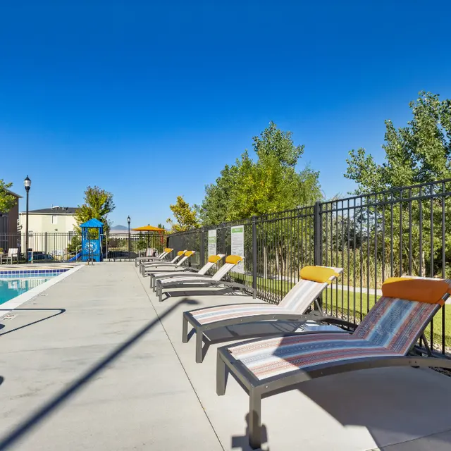 Sunny Poolside Lounge Area A bright, sunny poolside area featuring several lounge chairs along a swimming pool, surrounded by greenery and a fence.