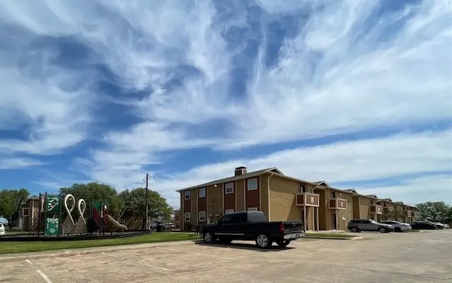 View of a residential apartment complex with a playground in the foreground under a cloudy sky.