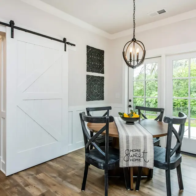 Modern dining room with a round table, black chairs, and a sliding barn door, featuring a simple decor and natural light.