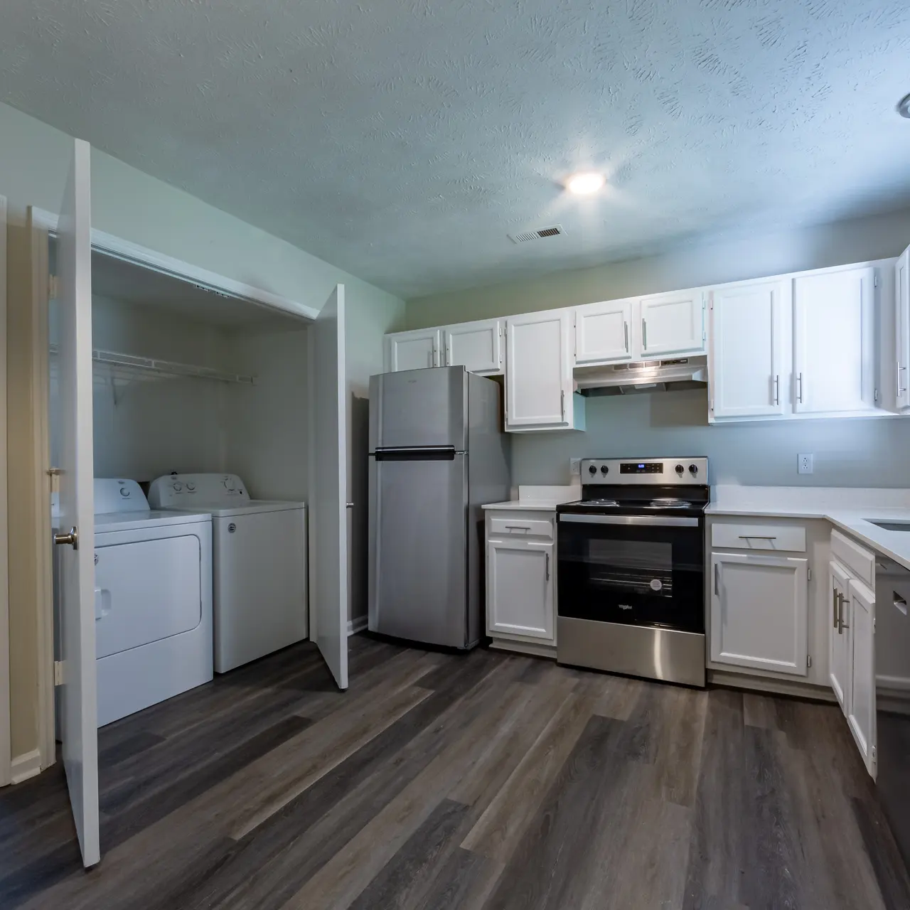 A modern kitchen featuring white cabinets, stainless steel appliances, and a laundry area visible through an open door.