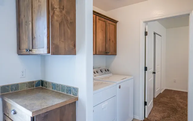 Cozy Laundry Room A laundry room with a washer and dryer, wooden cabinets, and a countertop. The space is well-lit and has a door leading to another room.