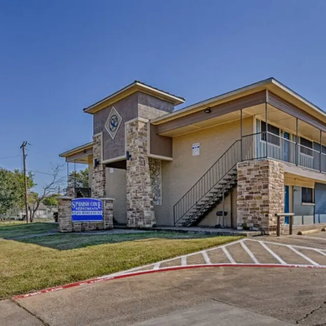 Exterior view of a two-story apartment building with a staircase and grassy area.