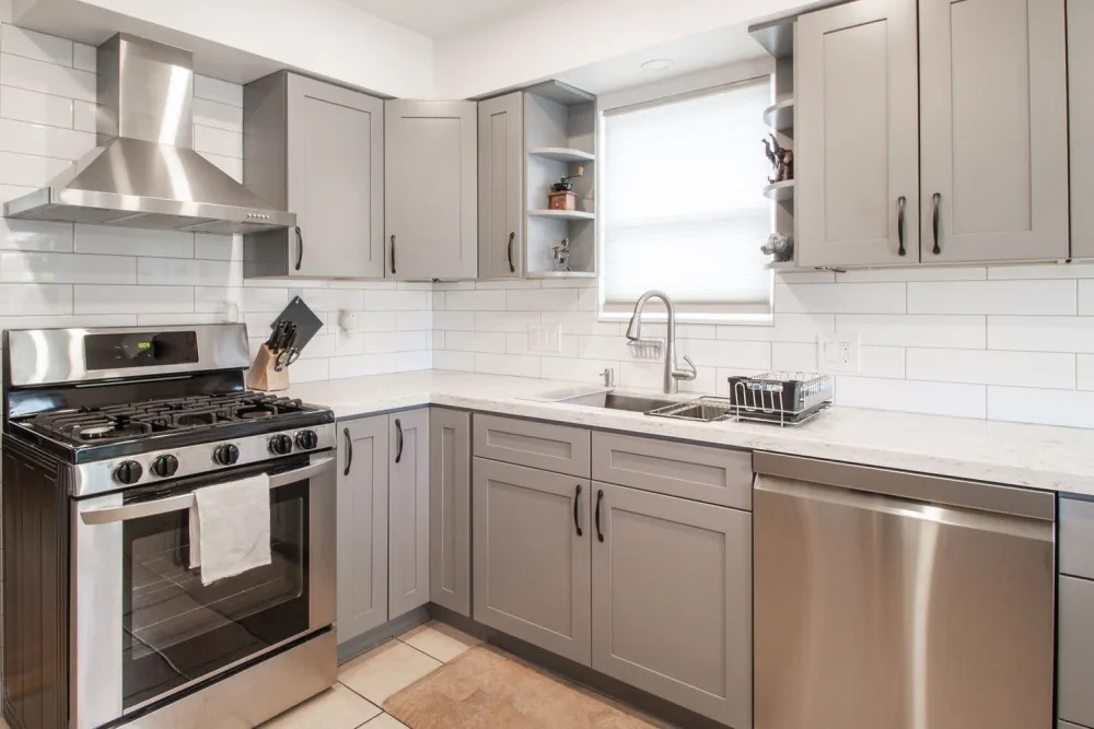 A modern kitchen featuring gray cabinets, stainless steel appliances, and white tiled backsplash.