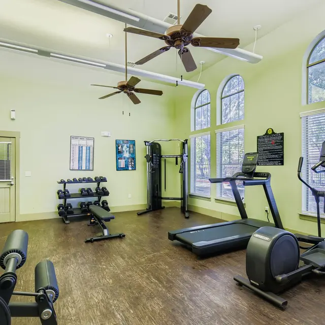 An indoor gym with exercise equipment and ample natural light coming from large windows.