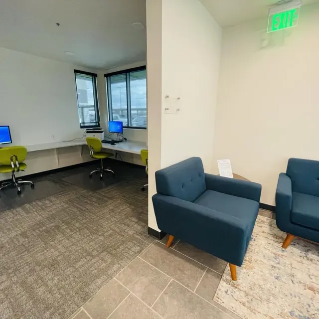Modern Office Space A modern office space featuring a small lounge area with a blue sofa, and a workspace with two computers and green chairs in the background.