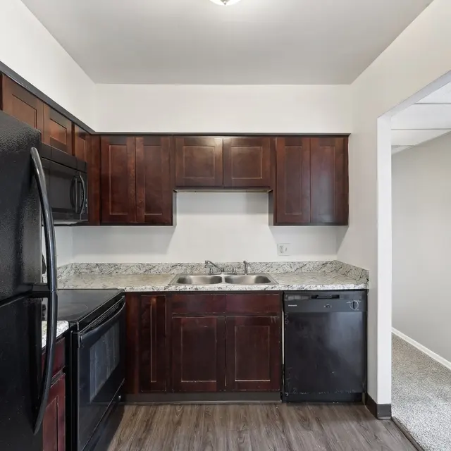 View of a modern kitchen with dark wooden cabinets, stainless steel appliances, and a granite countertop.