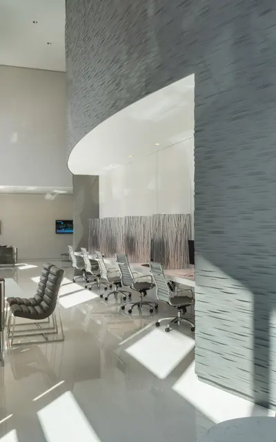 A modern office interior featuring sleek design with a large open space, bright lighting, and contemporary furniture including office chairs and desks. There are screens on the wall, and the floor is shiny and white, contributing to a clean aesthetic.