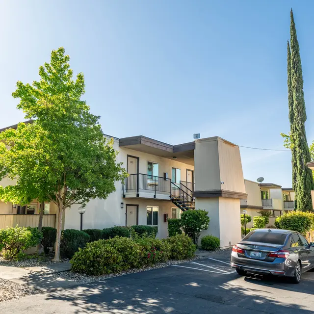 Exterior view of a modern apartment complex surrounded by greenery and parking spaces.