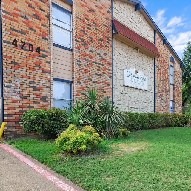 Exterior view of a multi-story apartment building with a brick and stone facade, surrounded by greenery and a lawn.