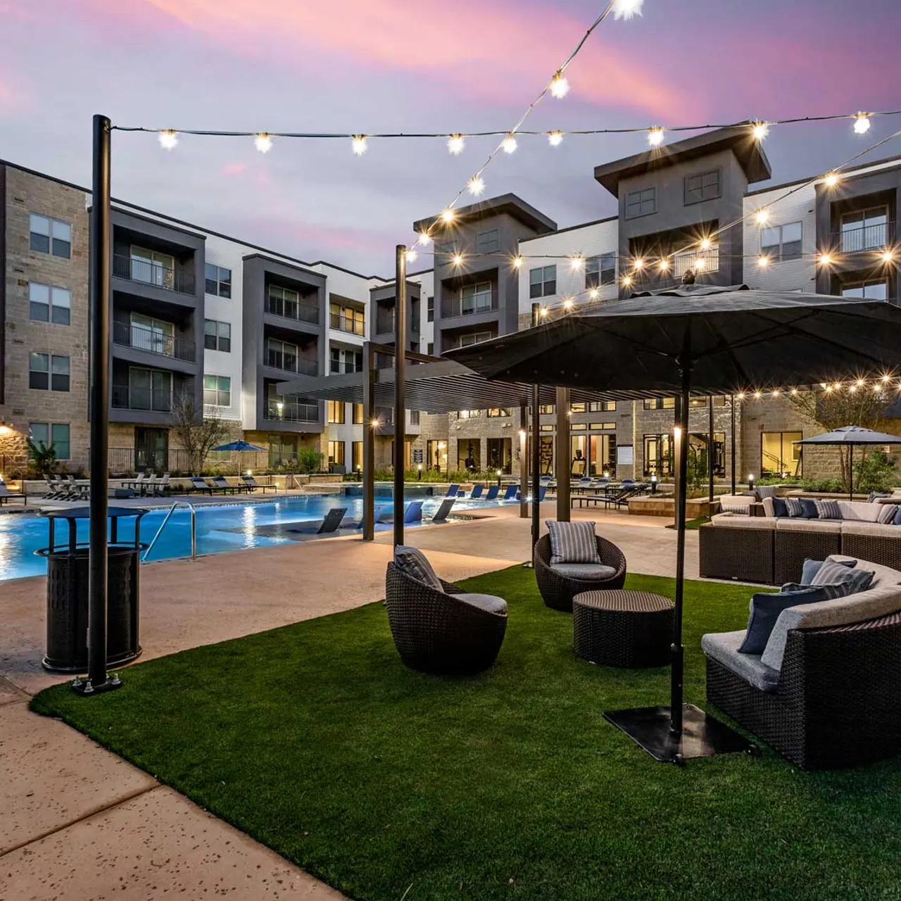Evening View of Apartment Pool Area A beautifully lit apartment pool area at dusk, featuring a swimming pool, modern seating, and light strings overhead.