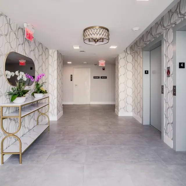 Modern elevator hallway with patterned wallpaper, gray tile flooring, and a decorative table with flowers.