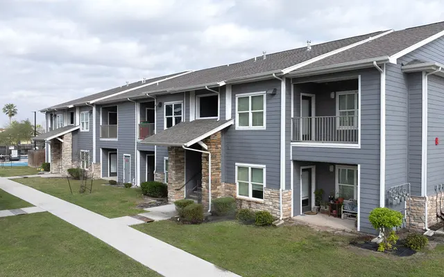 Exterior view of a modern apartment complex with a sidewalk, grassy area, and cloudy sky.