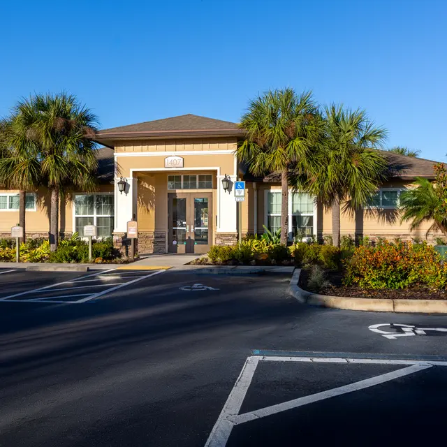 A modern community center building with palm trees and landscaped gardens in front, on a clear sunny day.