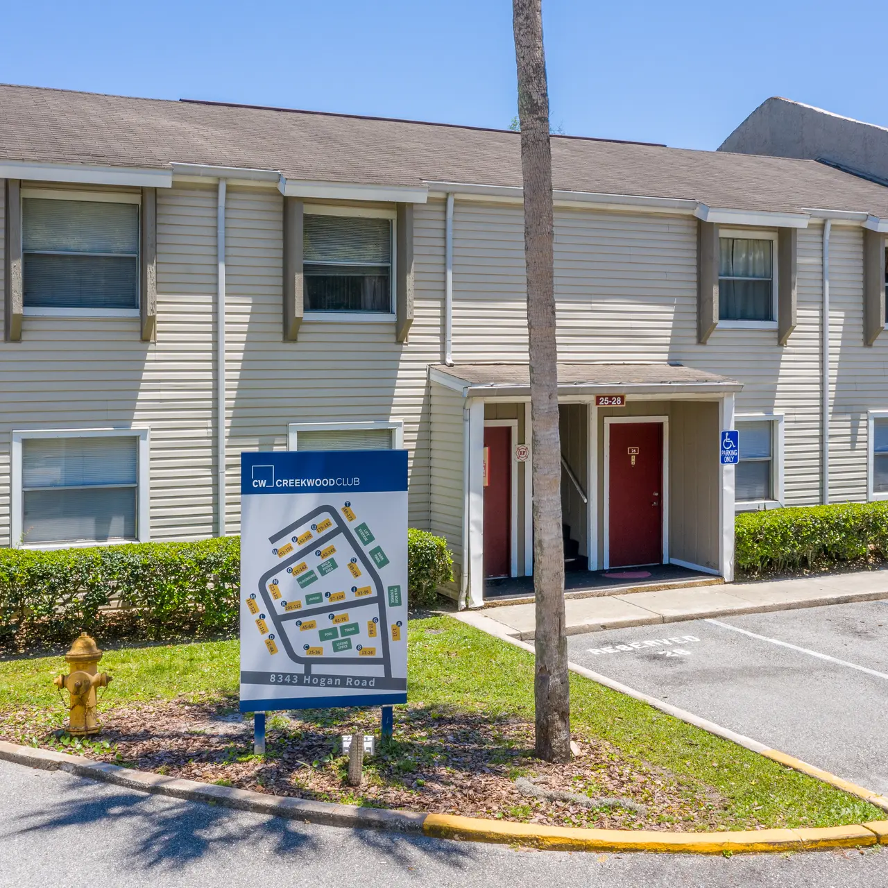 Exterior view of a two-story apartment building with a sign and parking spaces in front.