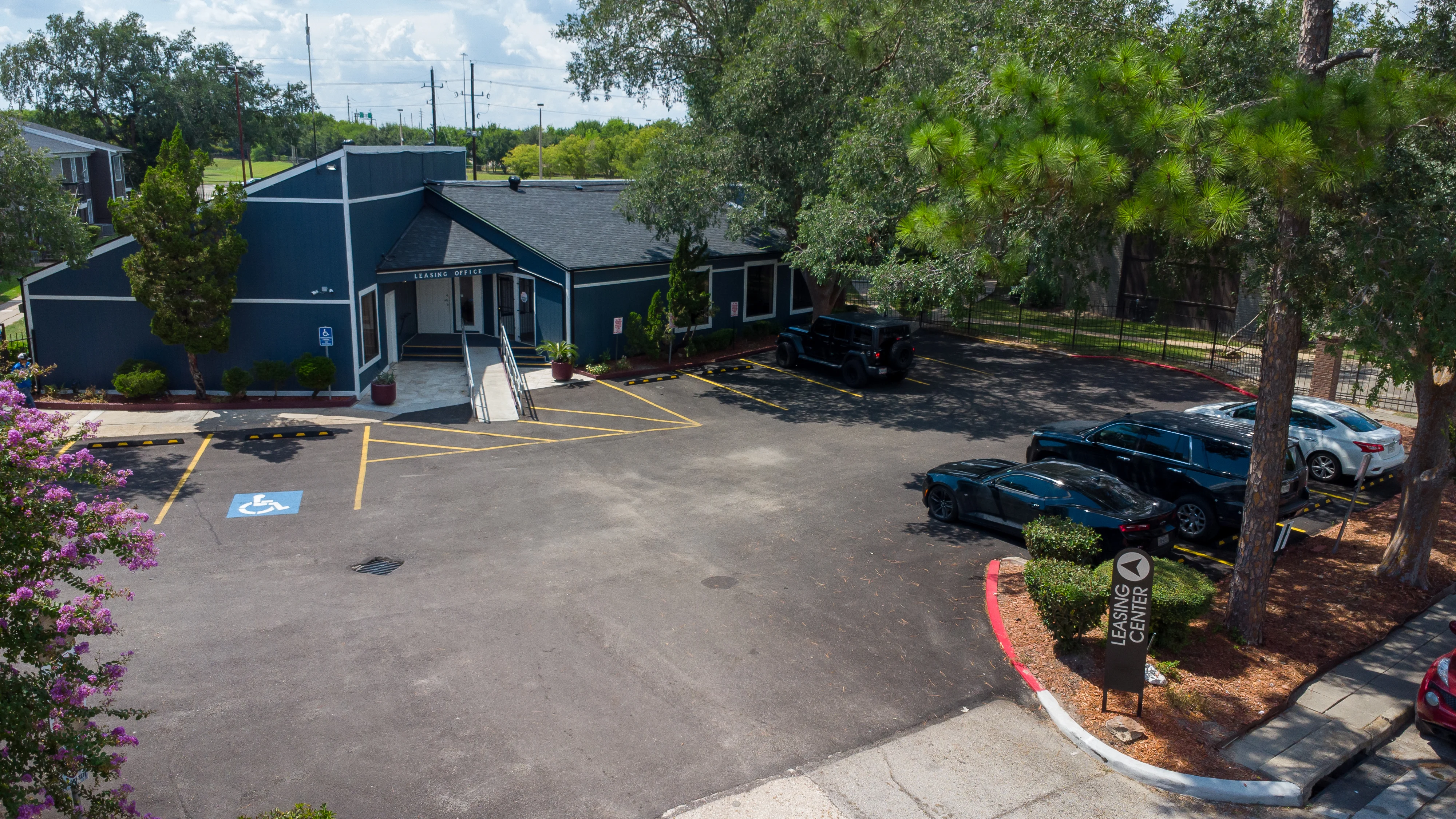 Aerial view of a blue building with a parking lot featuring several parked cars and trees nearby.