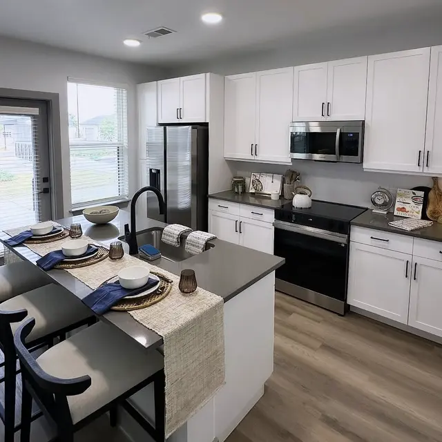 A modern kitchen featuring white cabinetry, a large island with seating, and stainless steel appliances. The space is bright with natural light coming through the window.
