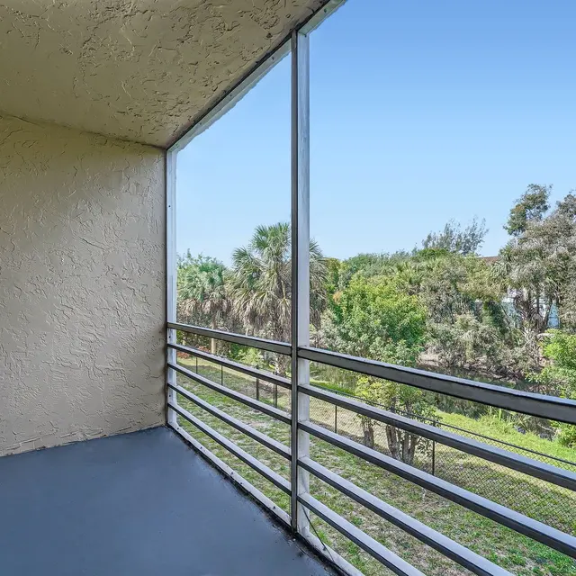 A spacious balcony with a gray floor and railing, overlooking green trees and vegetation.