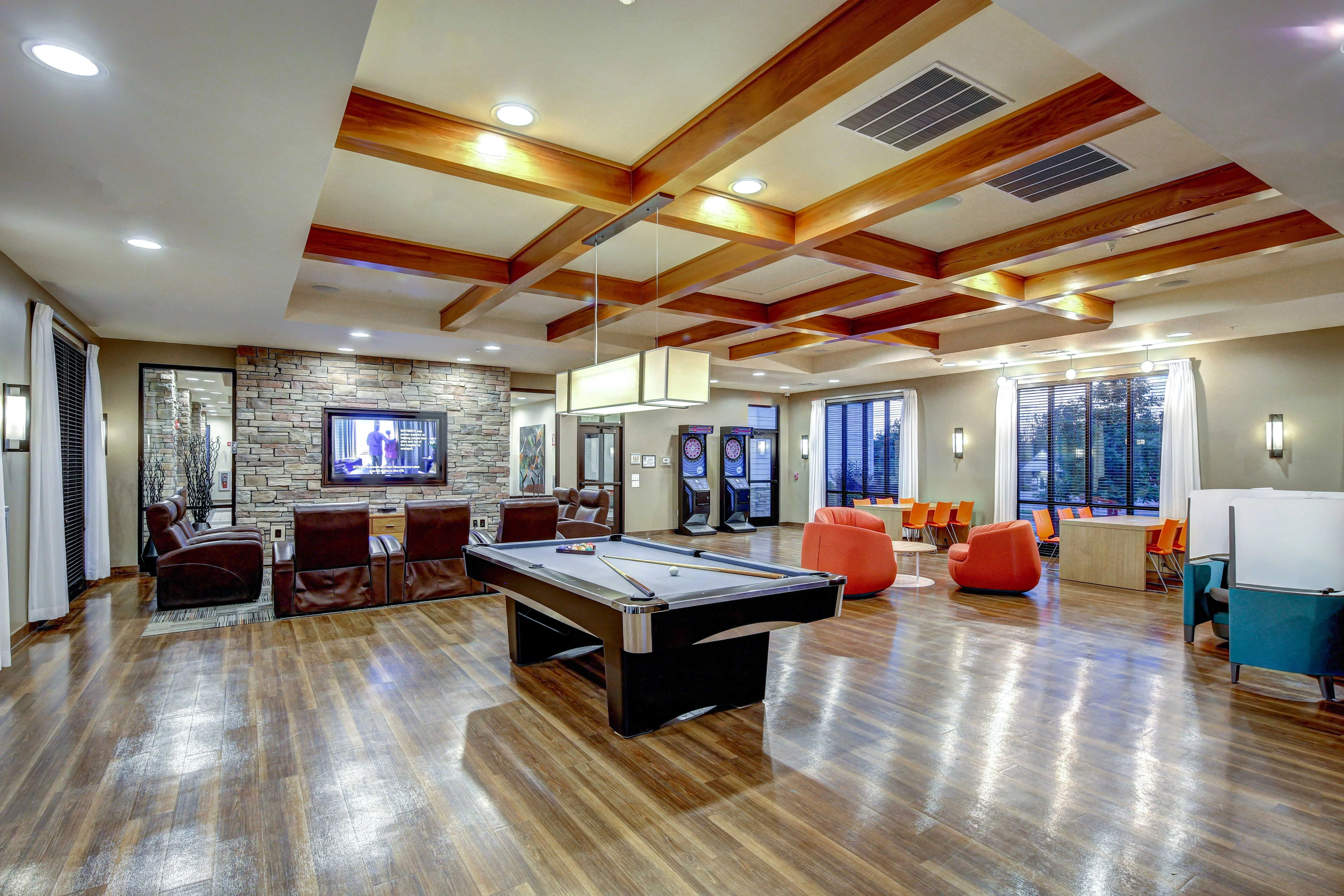 Modern Lounge Area with Pool Table A spacious lounge area featuring a pool table, modern furniture, and large windows allowing natural light to enter the room. The decor includes wooden beams and brick accents, creating a cozy atmosphere.