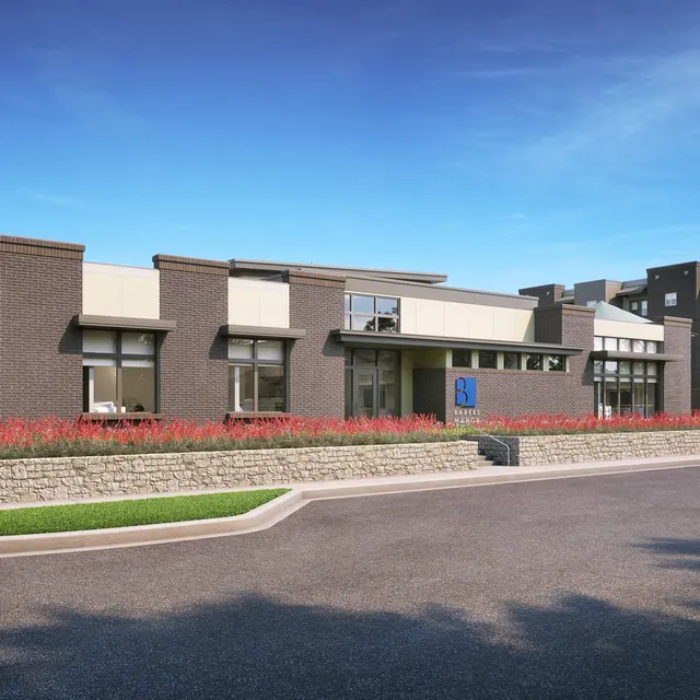 A modern building with a blend of brick and stucco exterior, featuring large windows and a landscaped front with colorful flowers.