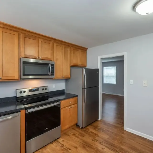 A modern kitchen with wooden cabinets, stainless steel appliances, and a hardwood floor.