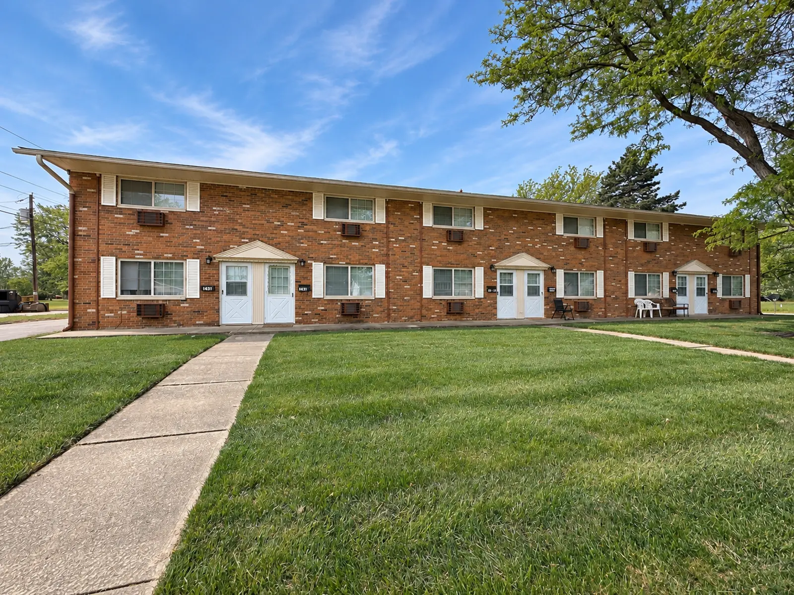 Exterior view of a two-story brick apartment building with green grass in front and a sunny sky.