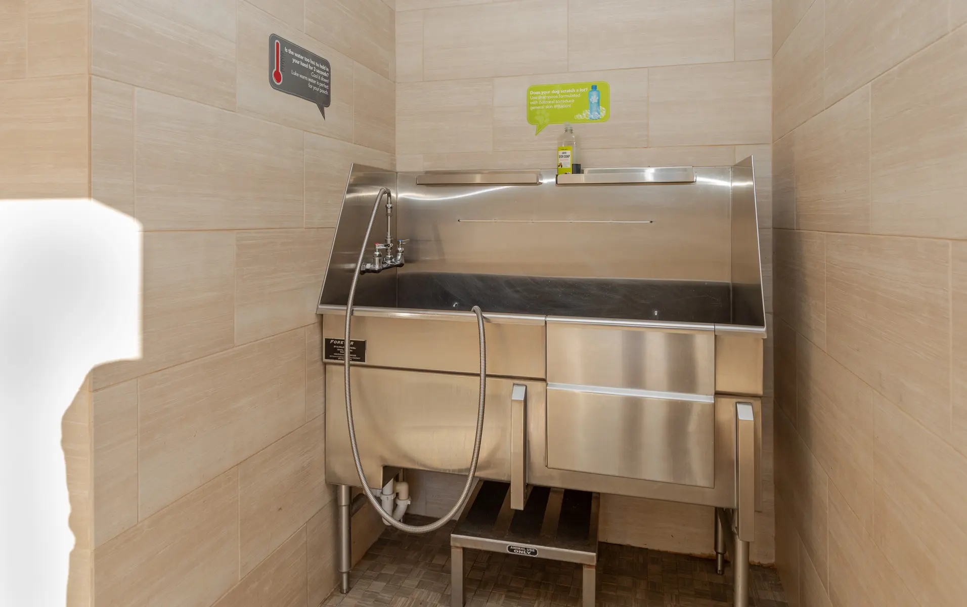 A stainless steel wash station with a faucet and a hose, situated in a tiled room with light-colored walls.