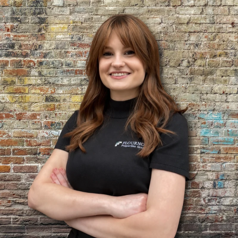 Portrait of a Woman A woman with long hair wearing a black shirt stands in front of a brick wall, smiling with arms crossed.