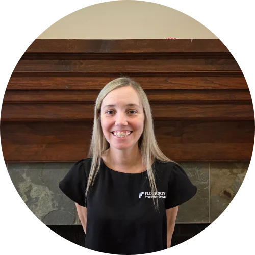 A woman with blonde hair smiles while standing in front of a wooden structure and a stone surface.