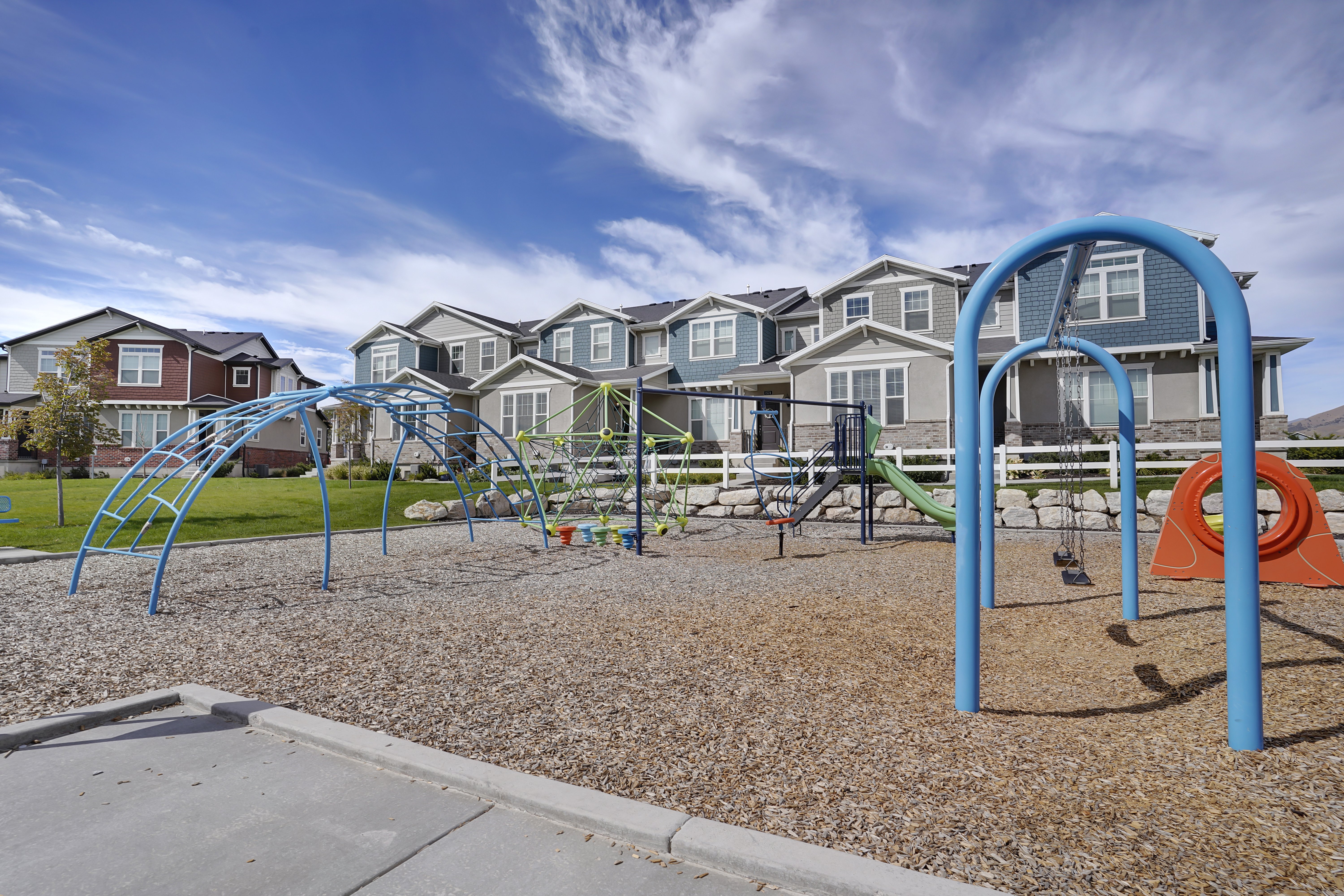 Playground in Residential Area A playground featuring climbing structures and swings in a residential neighborhood with townhouses in the background.