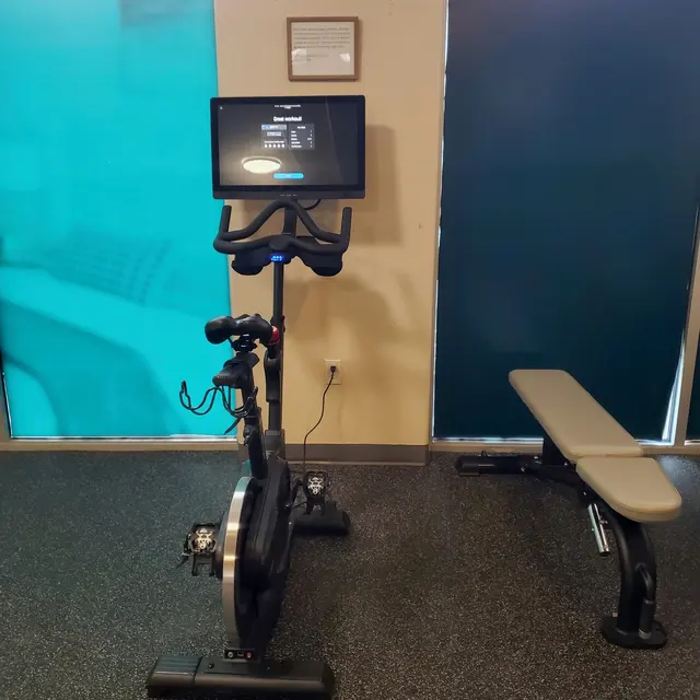 An indoor gym setup featuring an exercise bike with a monitor and a weight bench nearby.