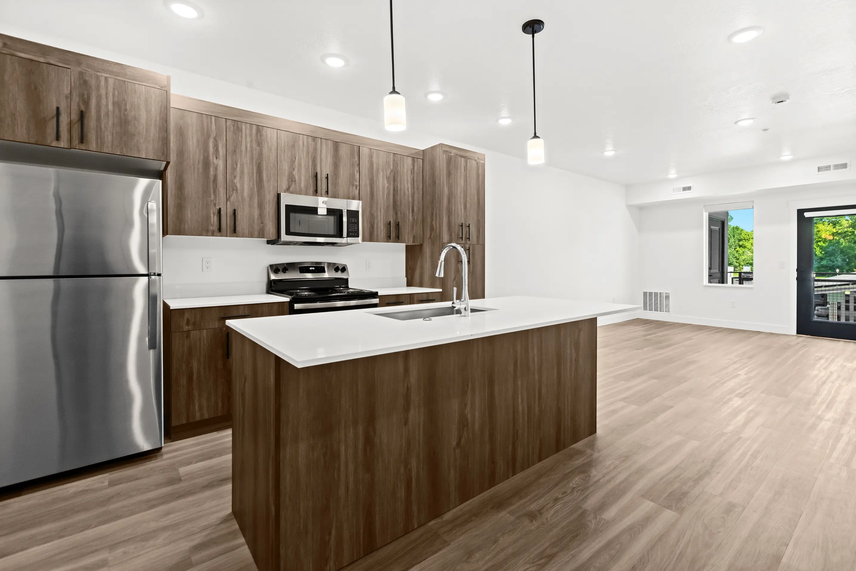 A modern kitchen featuring a central island, stainless steel appliances, wooden cabinets, and hardwood flooring.