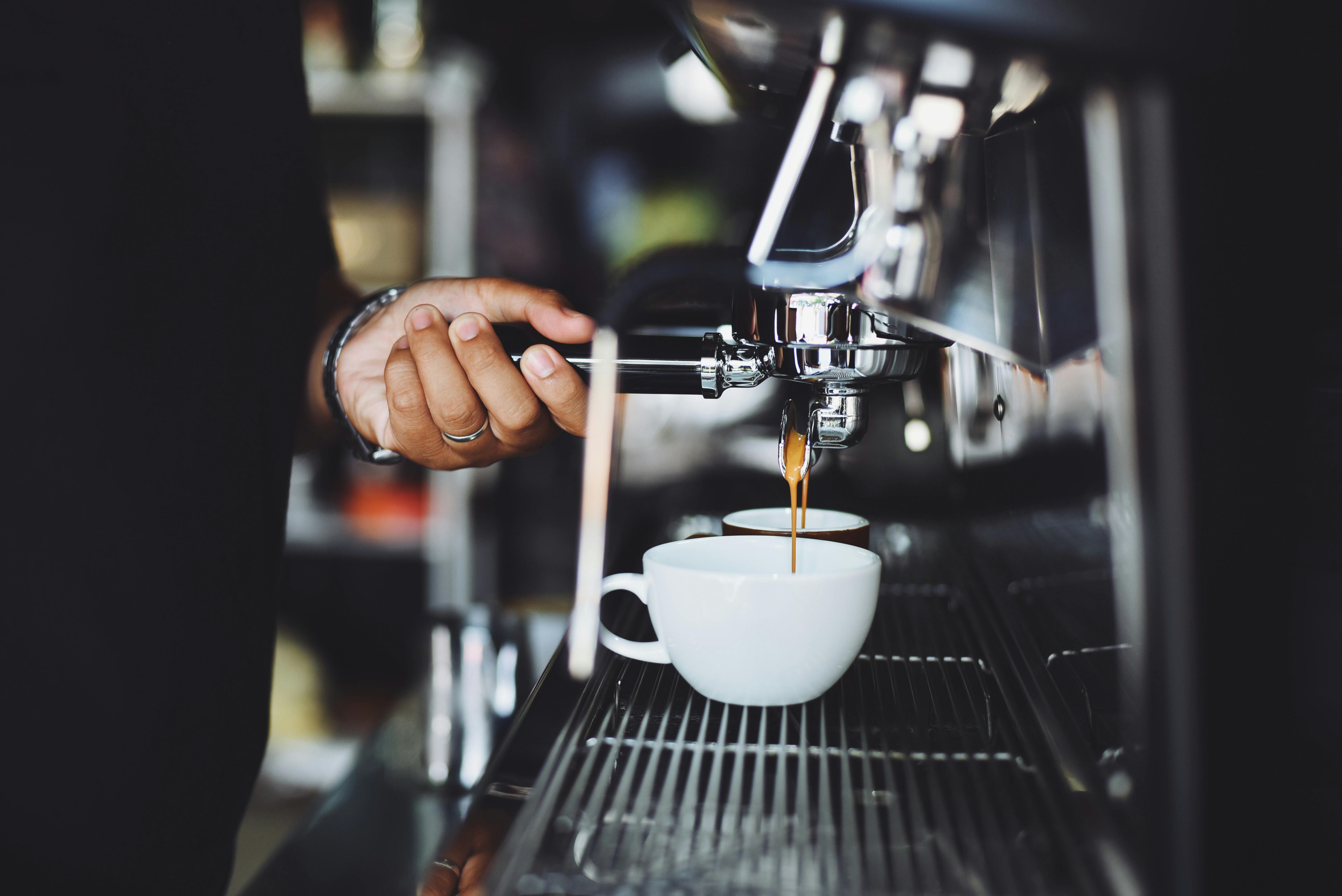 Riverstone Crossing A barista pouring fresh coffee into white cups from an espresso machine.