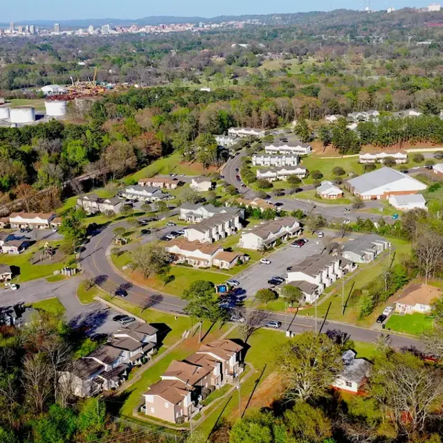 Aerial view of a suburban area surrounded by greenery, with curving streets and residential buildings.