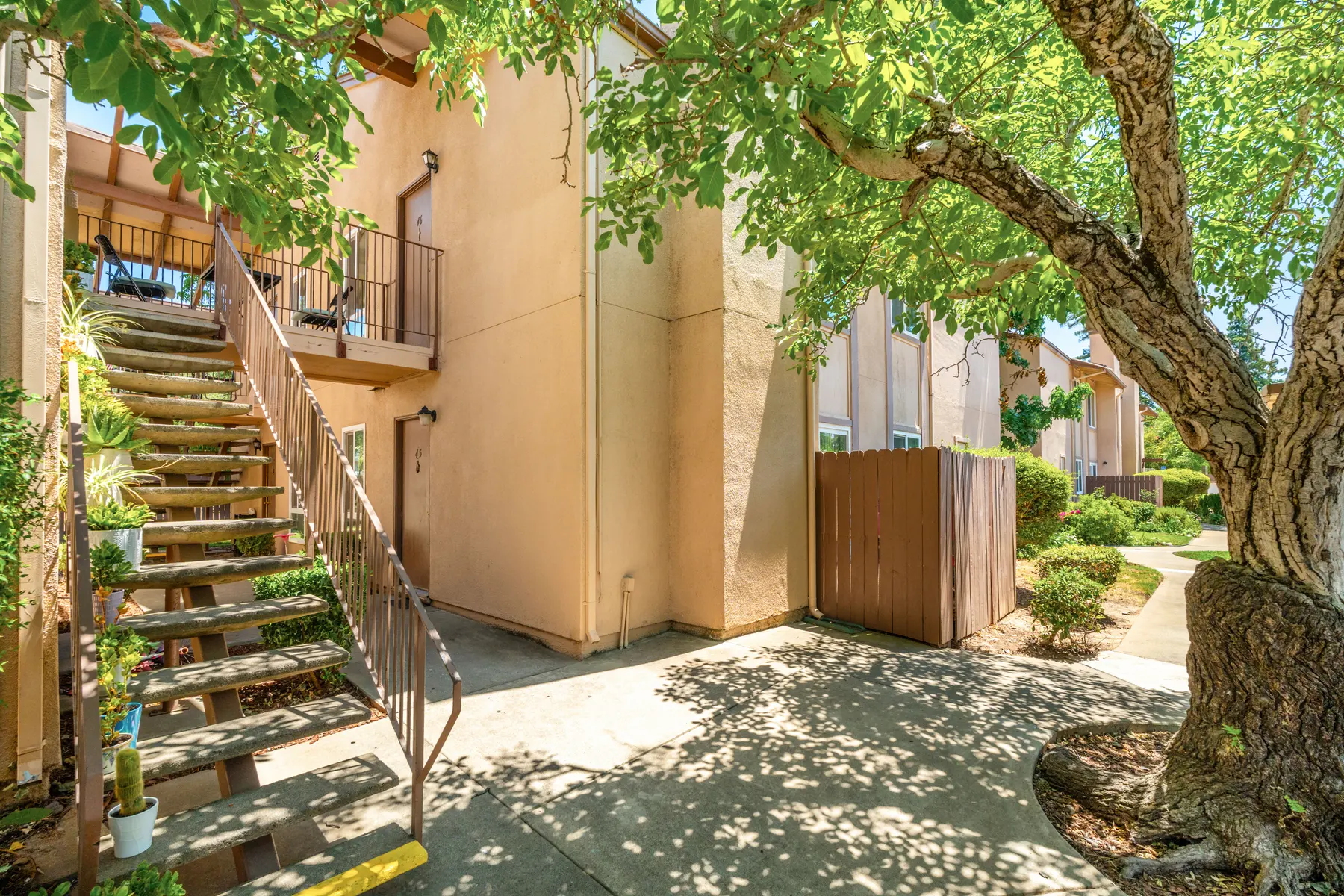 Exterior view of an apartment complex with a staircase, greenery and a spacious walkway.