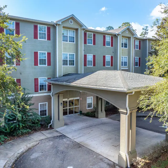 Front view of a multi-story apartment building with red shutters and landscaped surroundings.