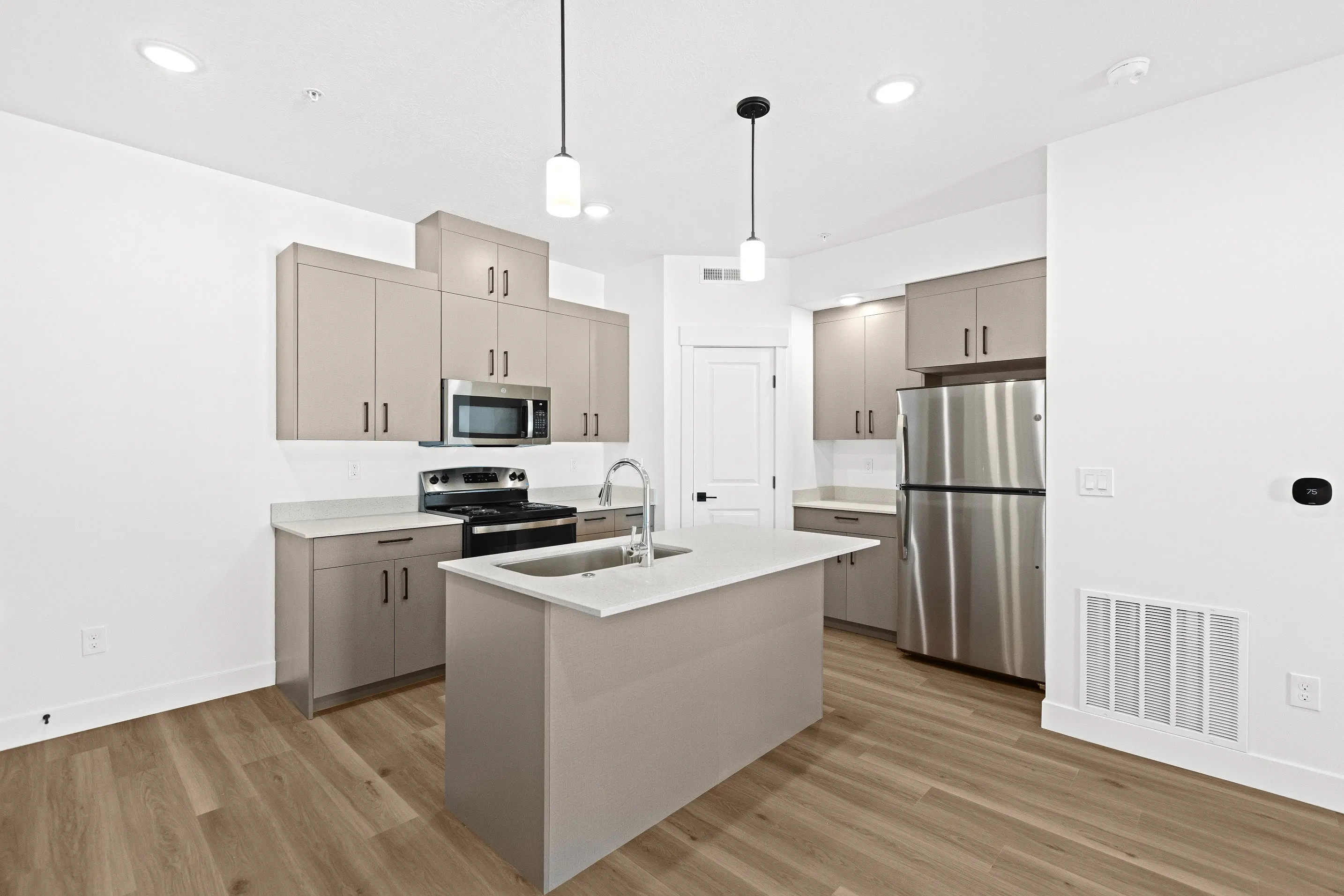 A modern kitchen featuring light brown cabinets, stainless steel appliances, a kitchen island with a sink, and wooden flooring.