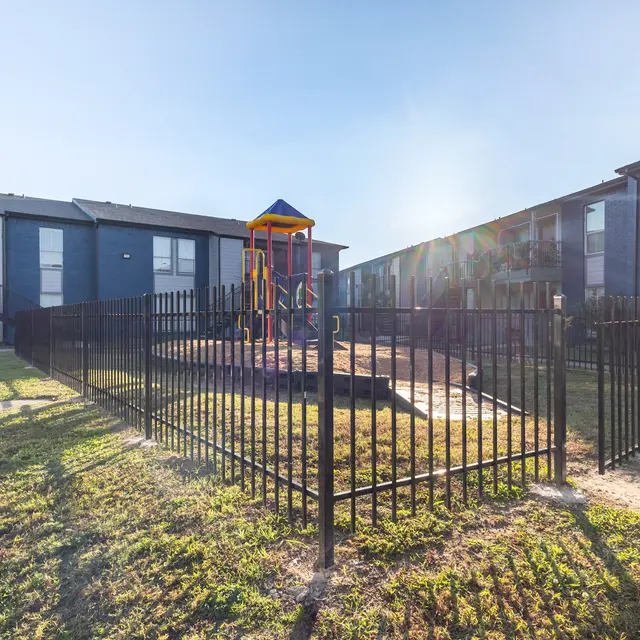 A fenced playground area with a colorful play structure, surrounded by apartment buildings.