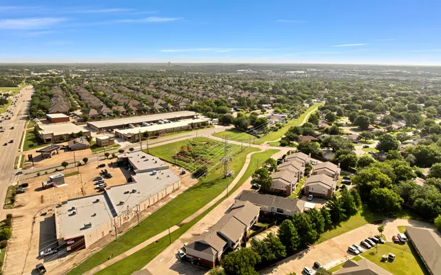 Aerial view of a suburban area featuring residential buildings, green spaces, and a main road.