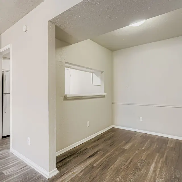 An empty living area with light colored walls, wooden flooring, and an open layout.