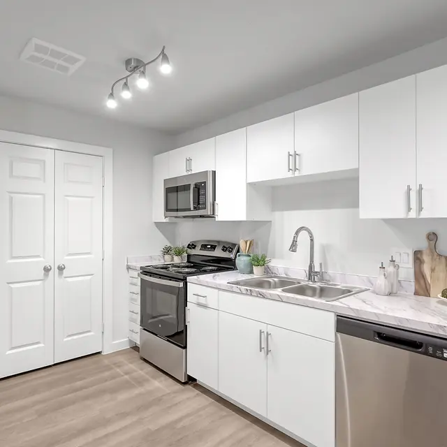 A modern kitchen featuring white cabinets, stainless steel appliances, a double sink, and a light countertop.
