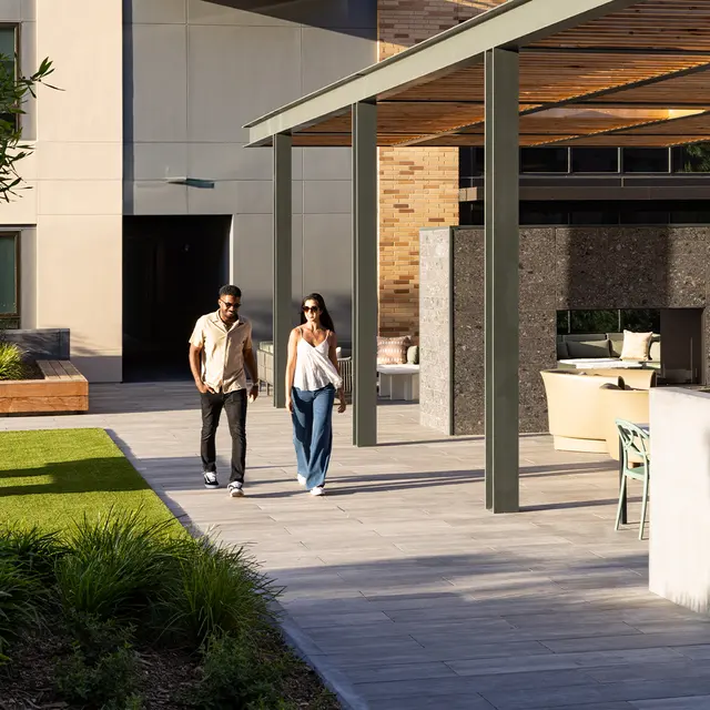A couple walking together in a modern outdoor space with greenery and contemporary architecture.