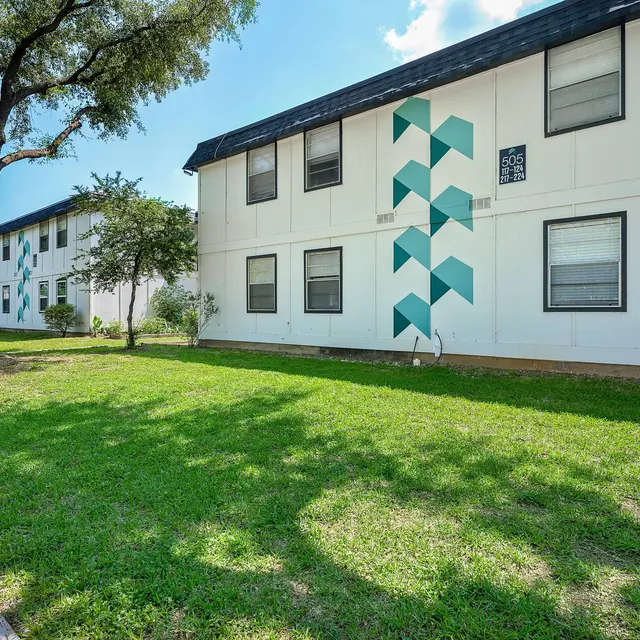 Two-story apartment building exteriors with geometric designs on one side, surrounded by grass and trees.