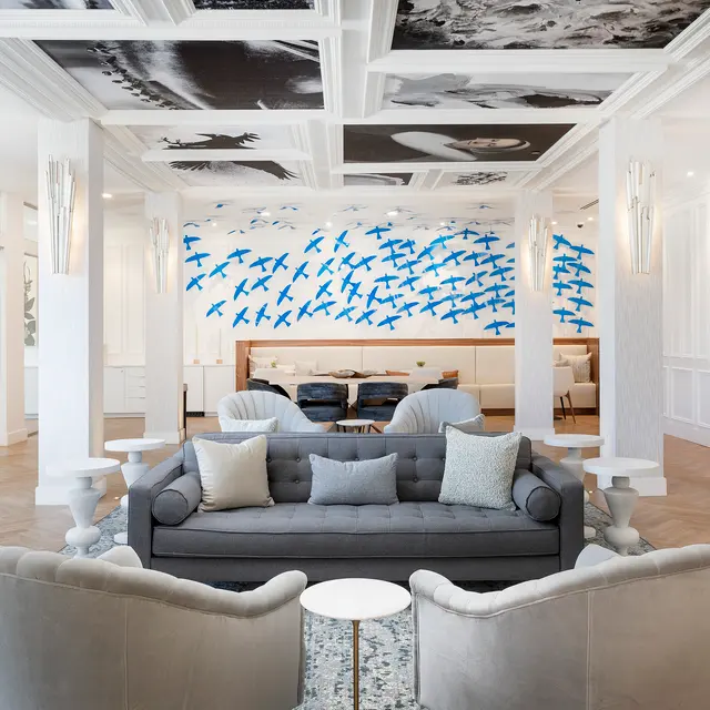 Modern lounge featuring a gray sofa, stylish armchairs, and a striking blue bird mural on the wall against a bright, airy backdrop.
