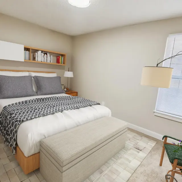 A modern, cozy bedroom featuring a double bed with gray bedding, two bedside lamps, and a stylish light fixture. There's a small bench at the foot of the bed and a chair with a green accent in the corner, along with a bookshelf mounted above the bed, holding decorative items. The room has neutral-colored walls and carpet, with natural light coming from a window.