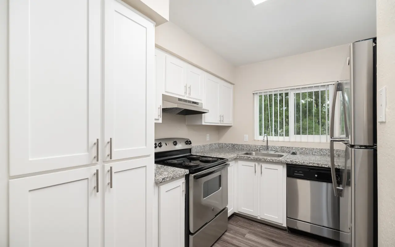 A modern kitchen featuring white cabinetry, stainless steel appliances including a stove, oven, and dishwasher, with a granite countertop and a window letting in natural light.