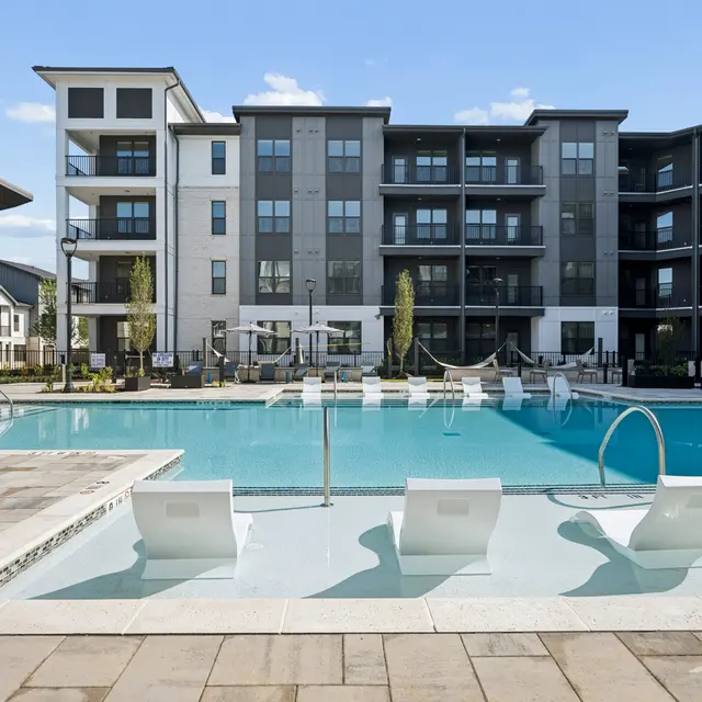 Modern Apartment Pool Area A modern apartment complex with a swimming pool surrounded by lounge chairs and a landscaped area.