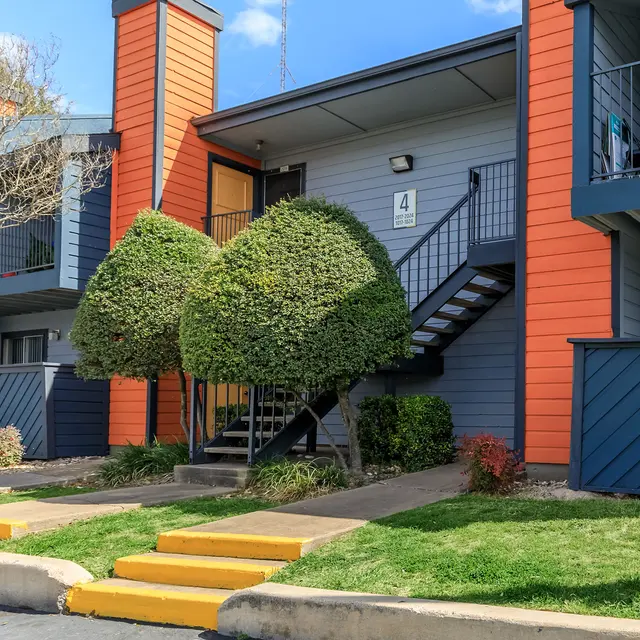 Exterior view of an apartment building with decorative shrubbery and a staircase.