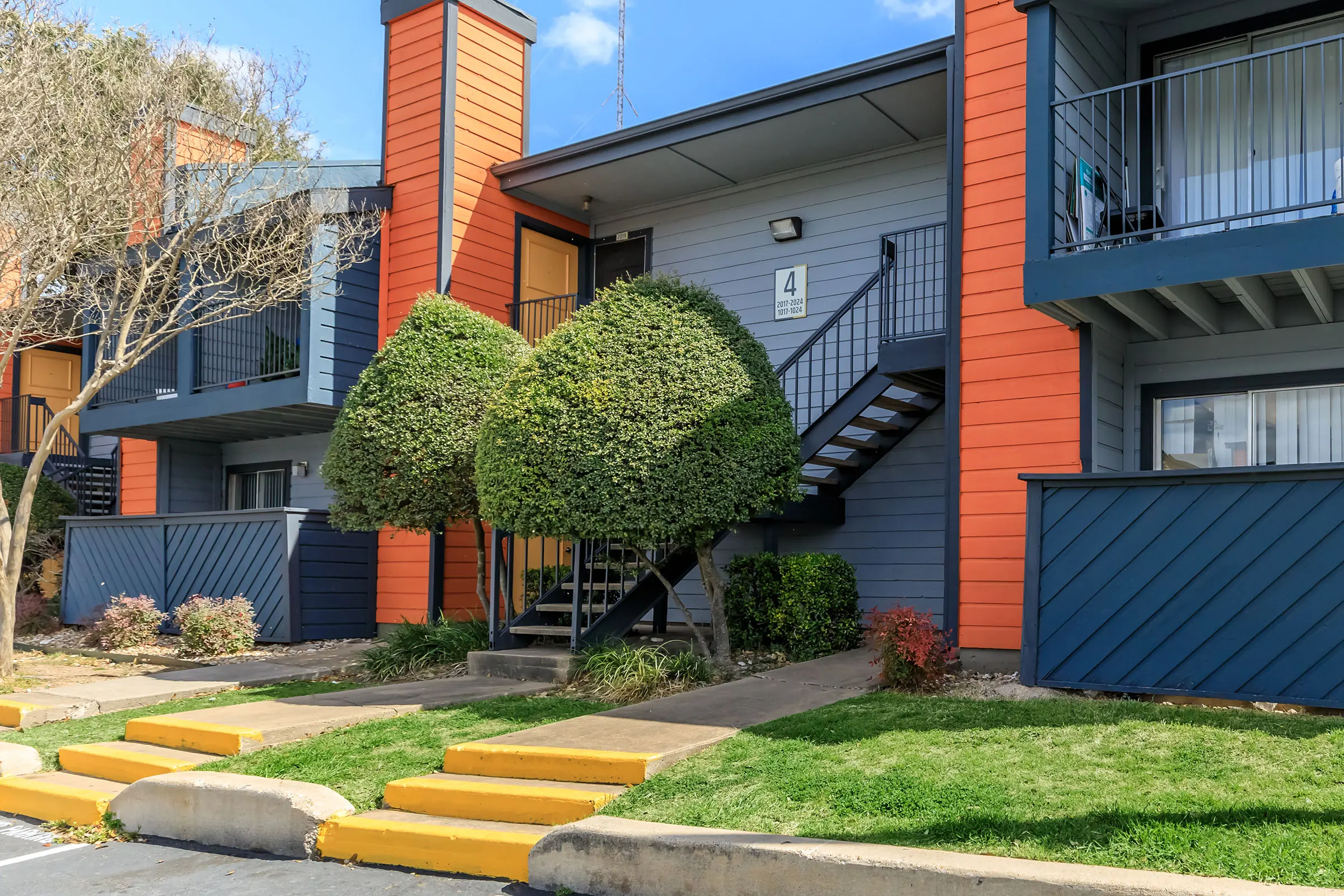 Exterior view of an apartment building with decorative shrubbery and a staircase.
