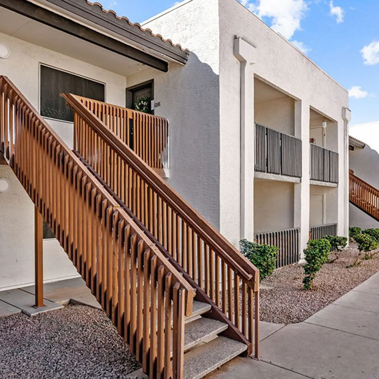 Exterior view of an apartment complex featuring wooden staircases and a pathway between buildings.