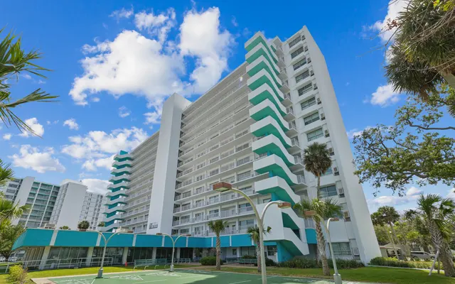 Tall hotel building with green and white architecture against a blue sky with fluffy clouds.